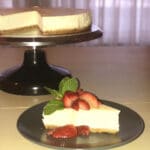 Delicious New York Style Cheesecake slice on a gray plate with cheesecake in the background