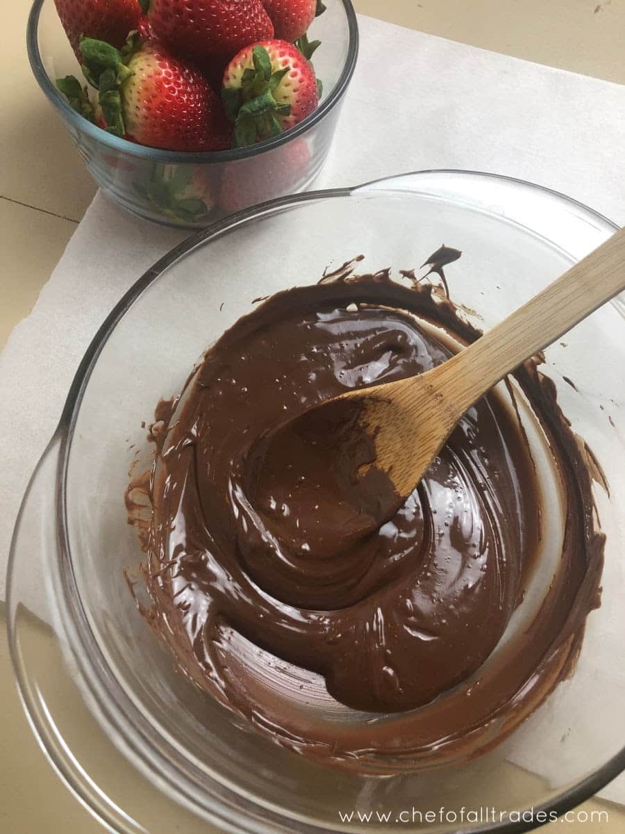 Melted chocolate in a bowl with a wooden spoon and a separate bowl of fresh strawberries