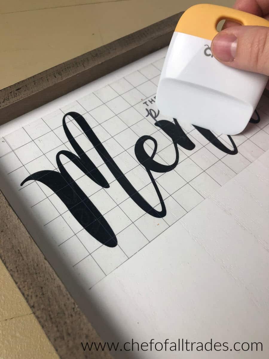 using a scraper to attach the vinyl to the menu board