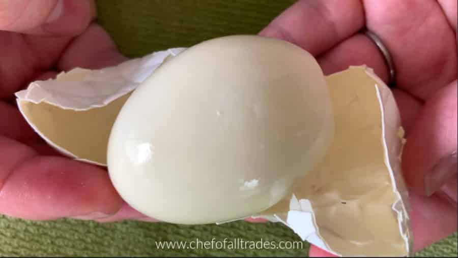 two hands peeling the broken shell off of a hardboiled egg