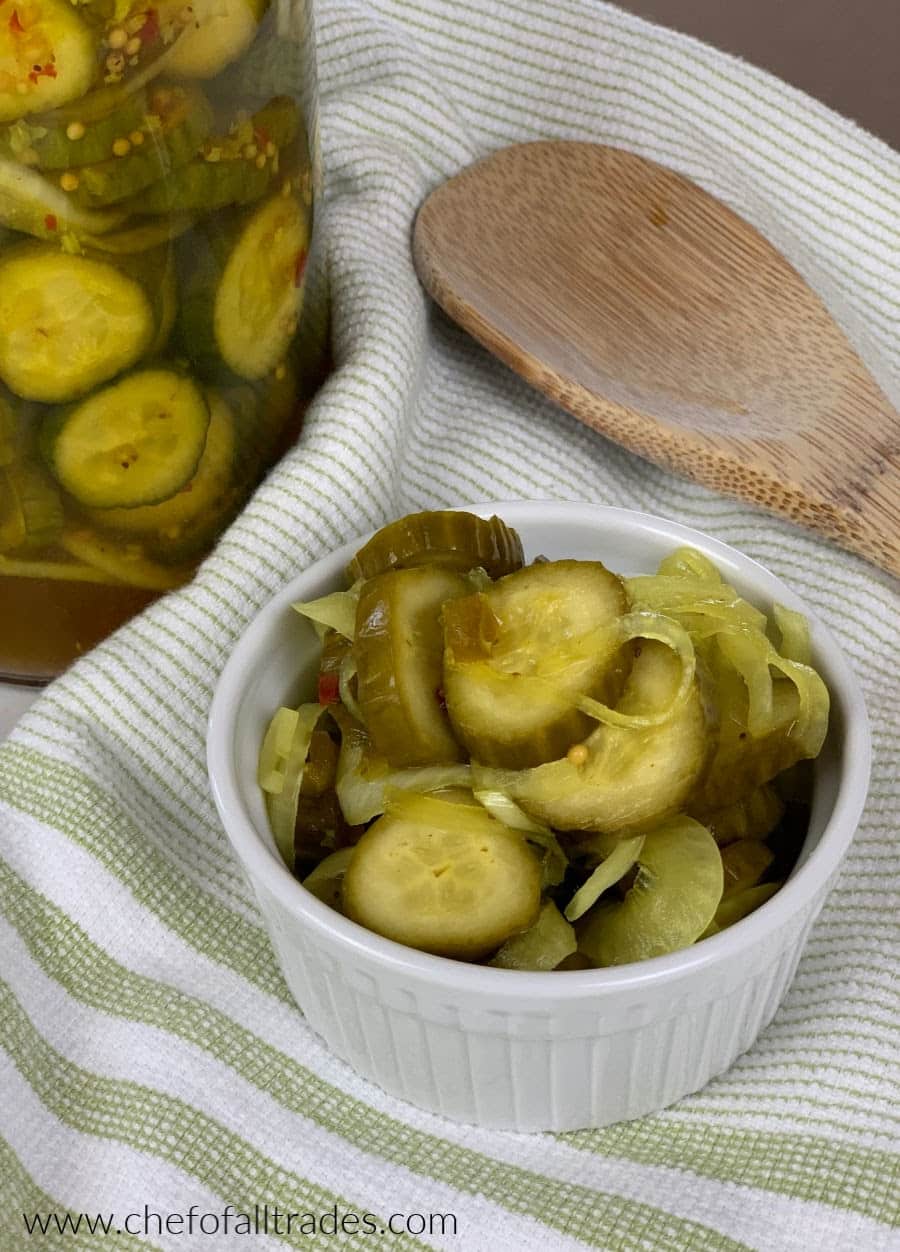 bread & butter pickles in a ramekin on a tea towel with pickles in a jar in the background