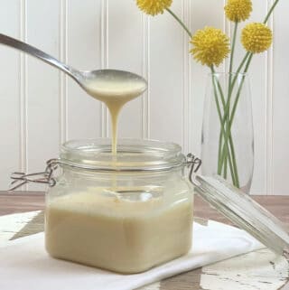 Sugar-Free Sweetened Condensed Milk in a mason jar in a cutting board with yellow flowers in the background