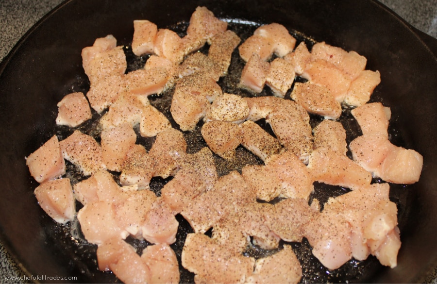 diced chicken in a skillet seasoned with salt and pepper