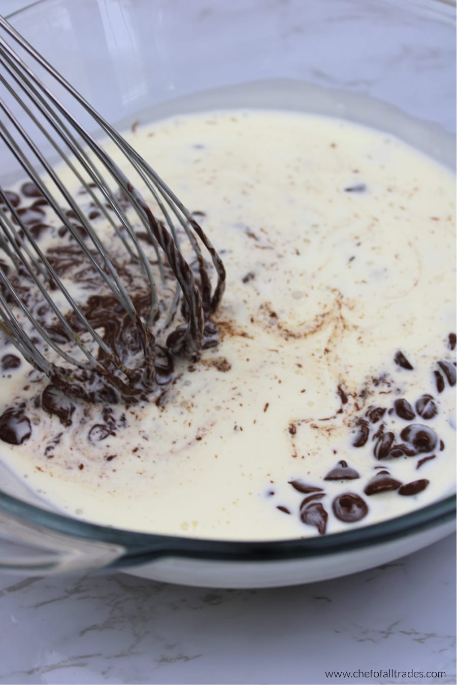 heavy cream and chocolate chips being whisked together in a glass bowl