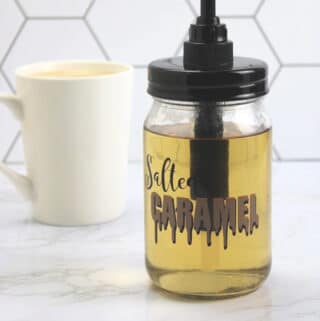 Salted Caramel Coffee Syrup in a mason jar with identifying label with a cup of coffee in the background