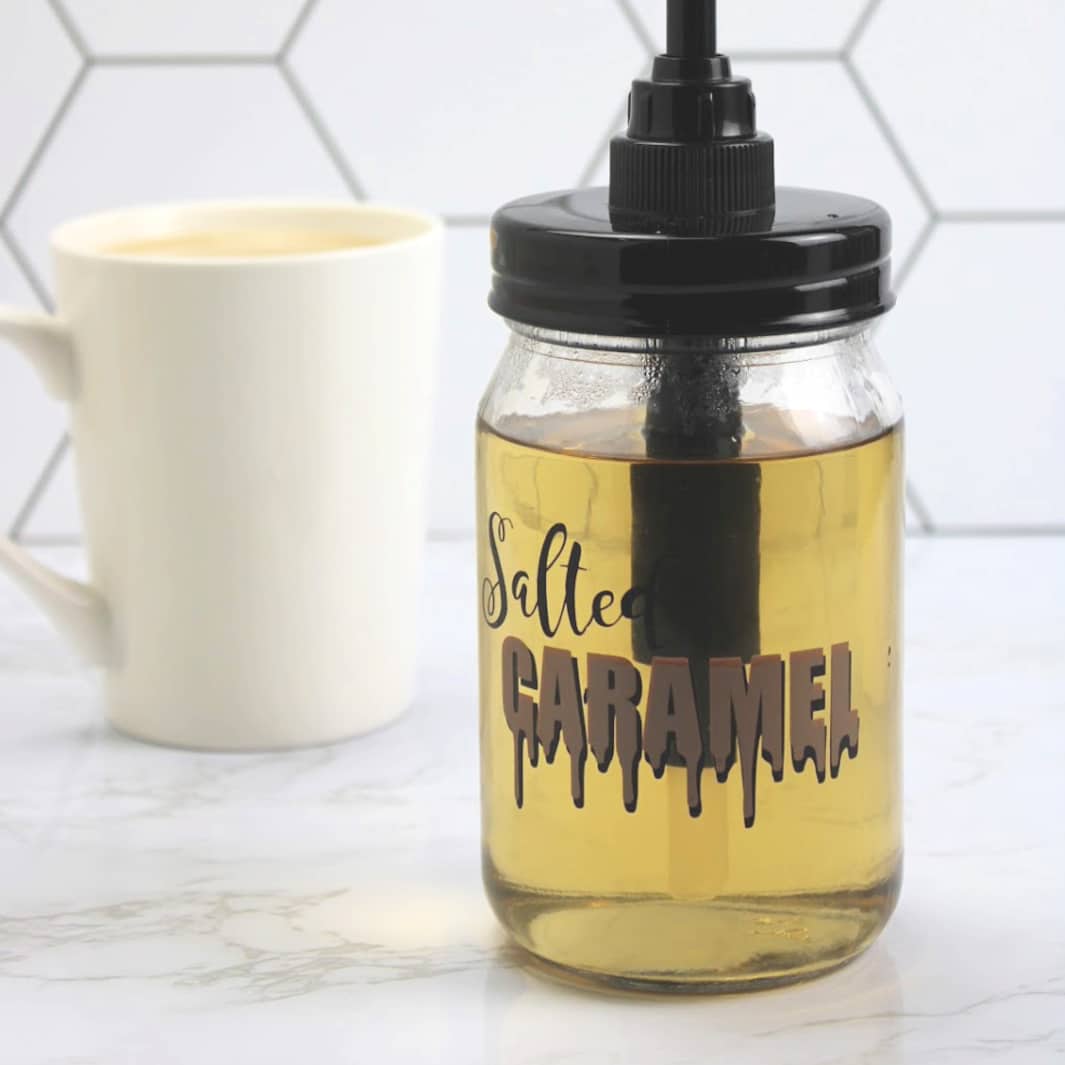 Salted Caramel Coffee Syrup in a mason jar with identifying label with a cup of coffee in the background