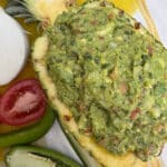 Guacamole in a hollowed out pineapple with the ingredients for guacamole surrounding the pineapple