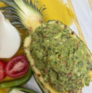 Guacamole in a hollowed out pineapple with the ingredients for guacamole surrounding the pineapple