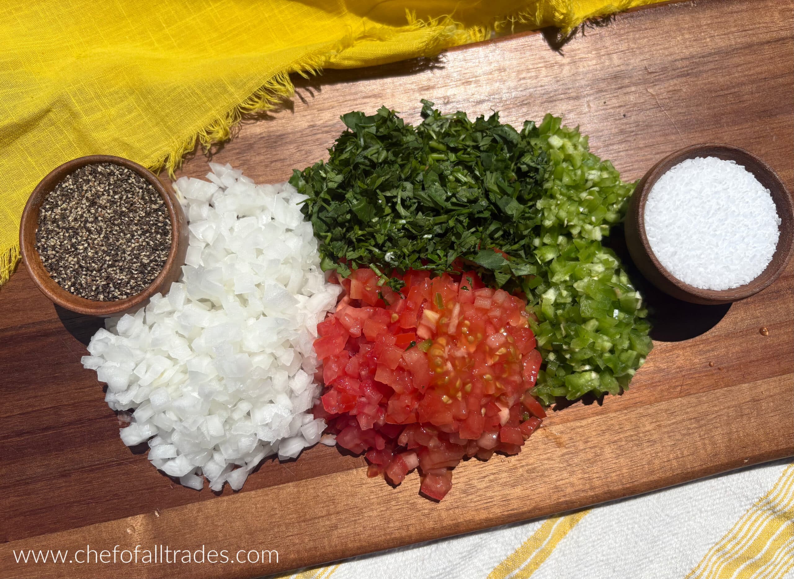 onion, jalapeno, serrano, cilantro, tomatoes finely diced on a wooden board with salt and pepper on either side.