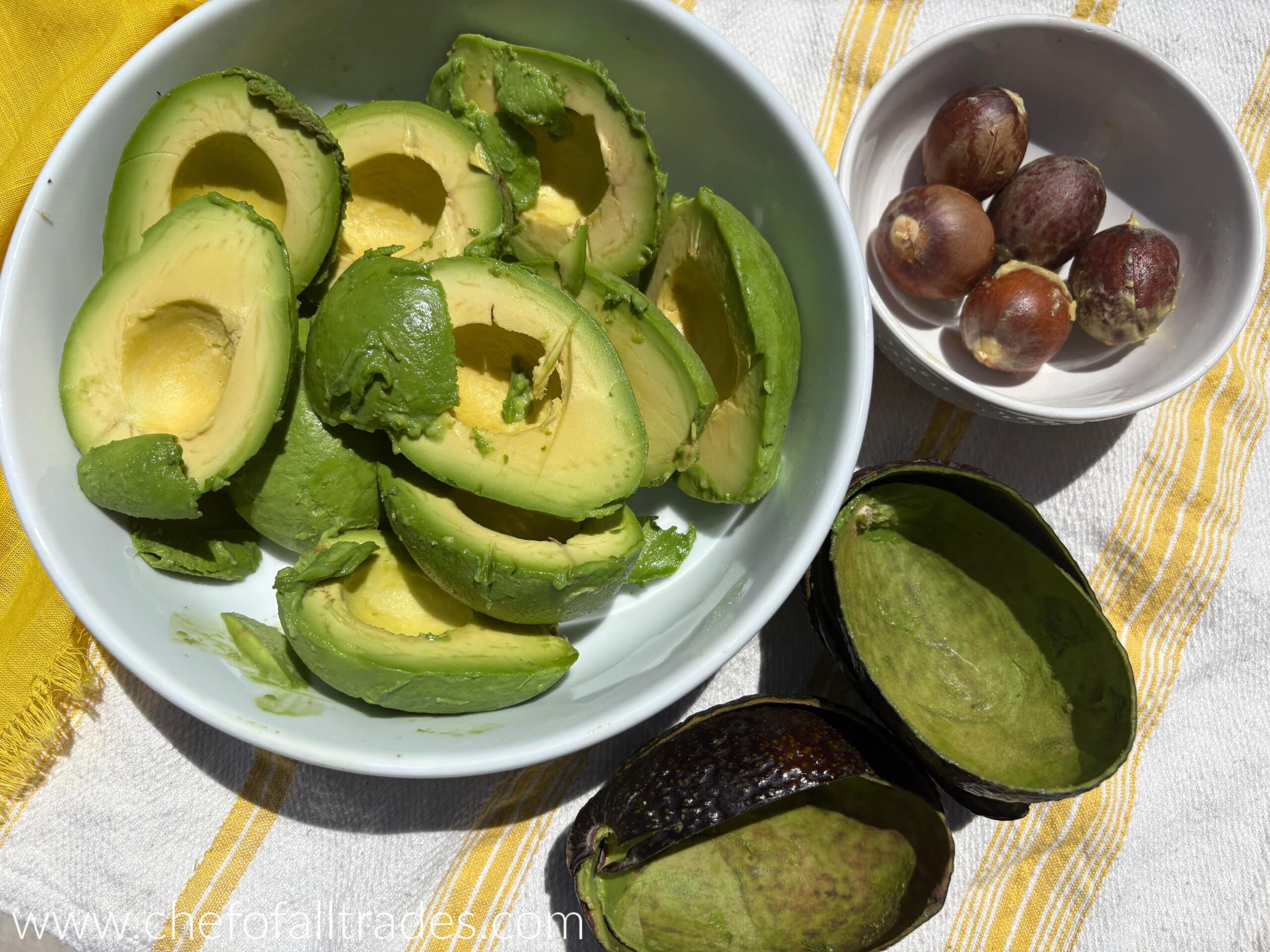 flesh of avocado scooped out of skins in a white bowl.
